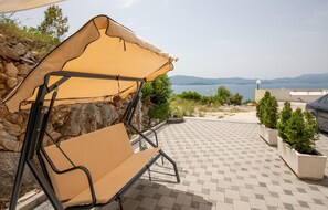 Une terrasse avec un fauteuil suspendu sous une pergola, un mur en pierre et une vue sur la mer.