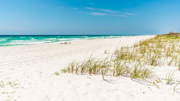 A beach with white sand, clear blue water, and sparse vegetation. - Blue Lagoon - Lakefront Getaway Private Pool, One Block to the Beach, Sleeps 12 (Panama City Beach)
