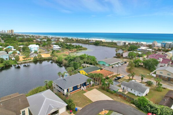 An aerial view of a residential area with houses, a river, and a beach in the background.