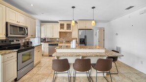 A modern kitchen with granite countertops, stainless steel appliances, and a central island with bar stools. - Blue Lagoon - Lakefront Getaway Private Pool, One Block to the Beach, Sleeps 12 (Panama City Beach)