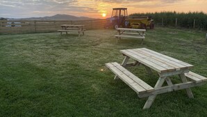 A picnic area with wooden benches and a tractor in the background during sunset. - Cosy Annexe Sleeps 4 (Holyhead)