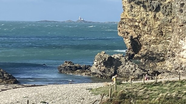 A rocky coastline with a lighthouse in the distance, a sandy beach, and a clear sky. - Cosy Annexe Sleeps 4 (Holyhead)