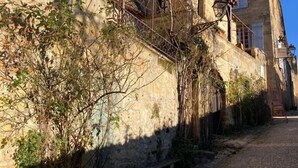 A narrow cobblestone street flanked by stone buildings with wooden shutters and a metal fence.
