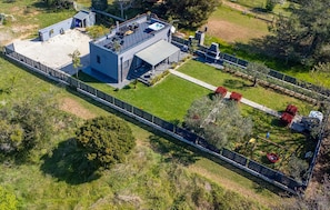 An aerial view of a modern house with a rooftop patio, a swimming pool, and a fenced garden area.