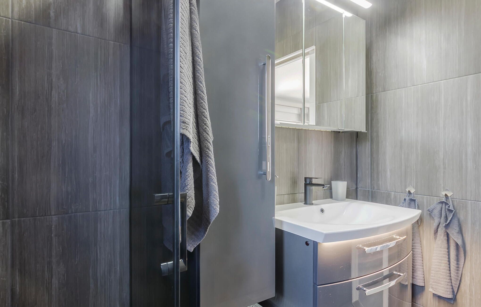 A modern bathroom with a large mirror, a white sink, and a towel rack.