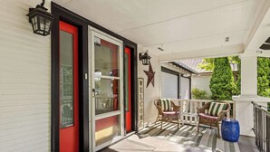 A covered porch with a red door, a wicker chair, a blue barrel, and a star decoration. - 5th St Bungalow - Historic Charm Near 3rd St (McMinnville)