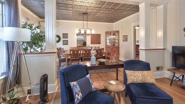 A spacious living room with a high ceiling, a dining area with wooden furniture, and a television on a wooden stand. - 5th St Bungalow - Historic Charm Near 3rd St (McMinnville)