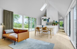 Relax in this open-plan living space with a leather sofa, dining area, and modern kitchen, seamlessly connecting indoors and outdoors.