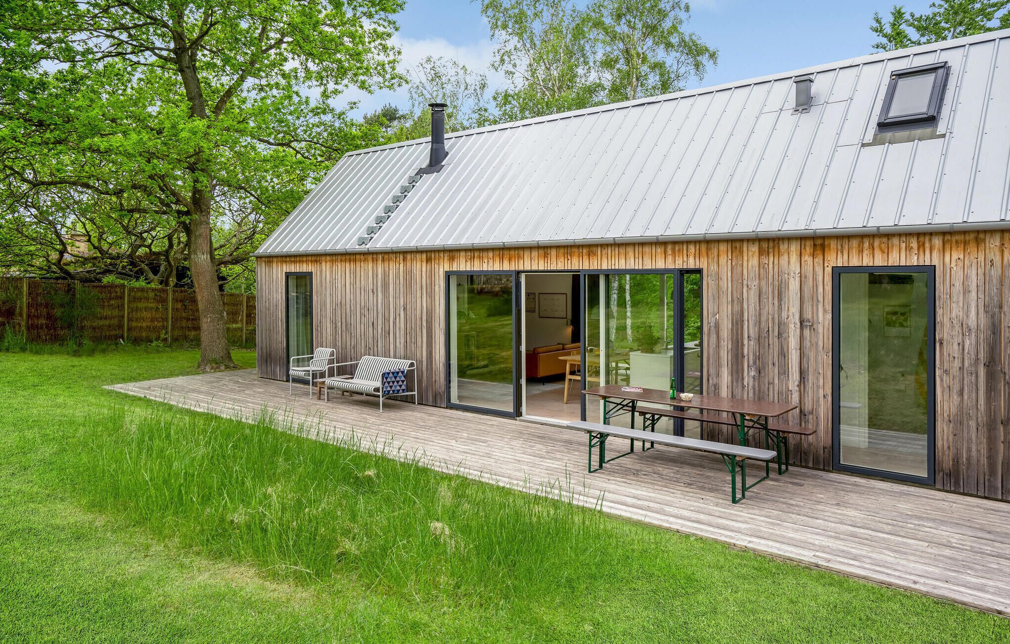 Ein modernes Haus mit Holzterrasse, Schiebeglastüren und einem Metalldach.