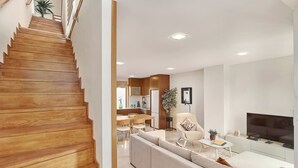Un salon moderne avec un escalier en bois, un canapé, un téléviseur et un coin repas.
