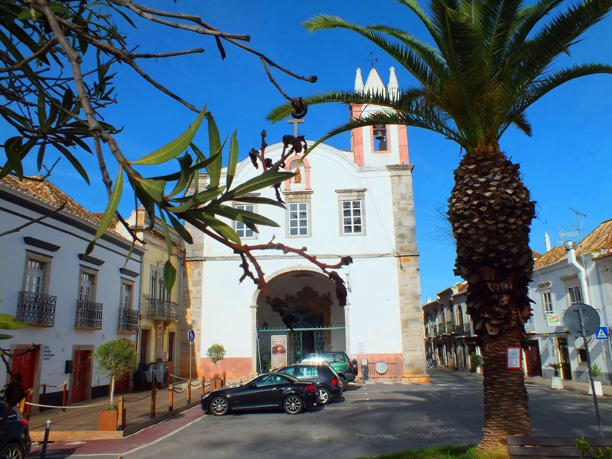 A street view with a church featuring a bell tower and a palm tree.