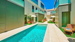 Ein moderner Hotelinnenhof mit Swimmingpool, Liegestühlen und Topfpflanzen.