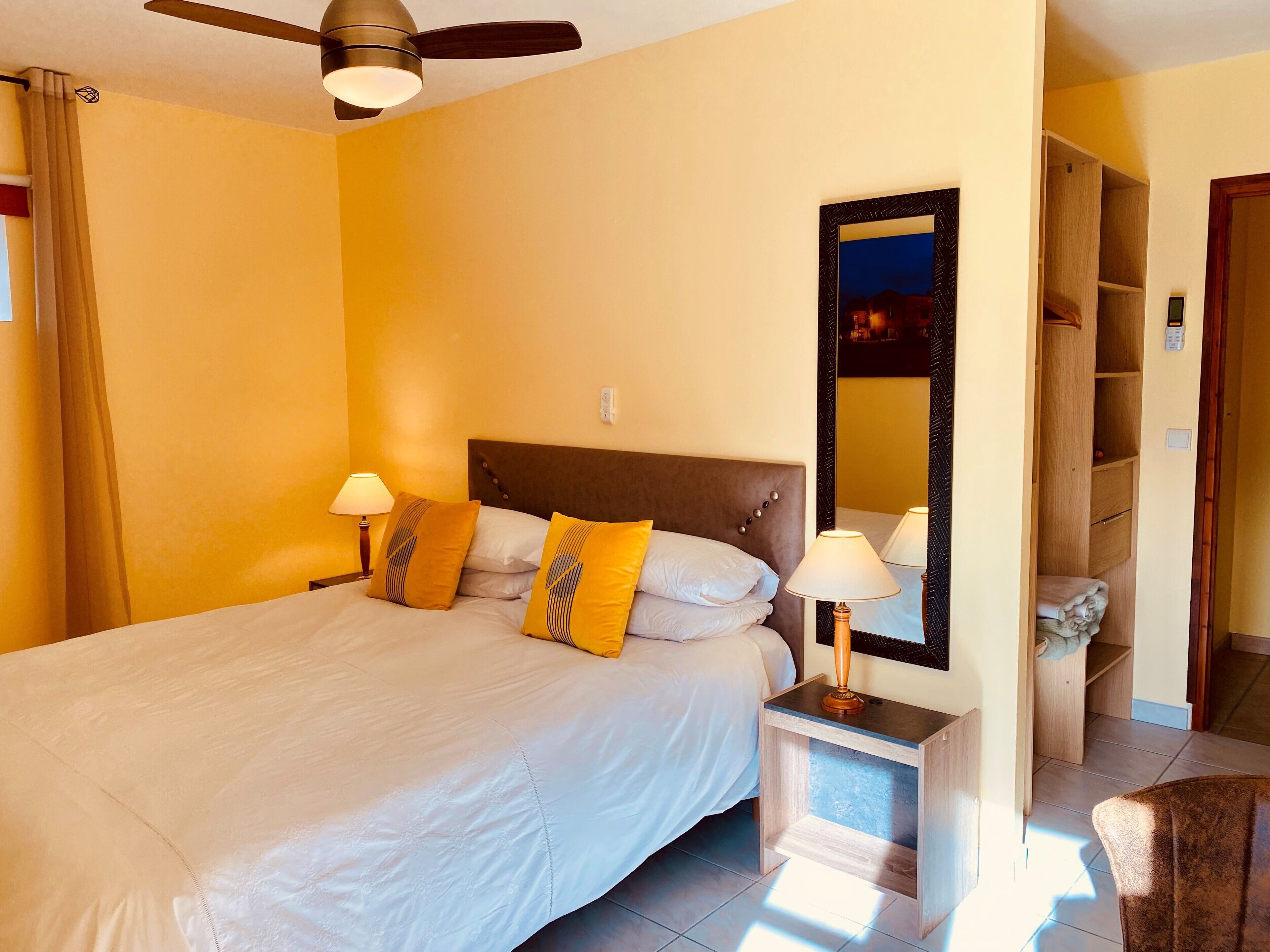 Un grand lit avec deux tables de chevet, un ventilateur de plafond et un miroir au mur.