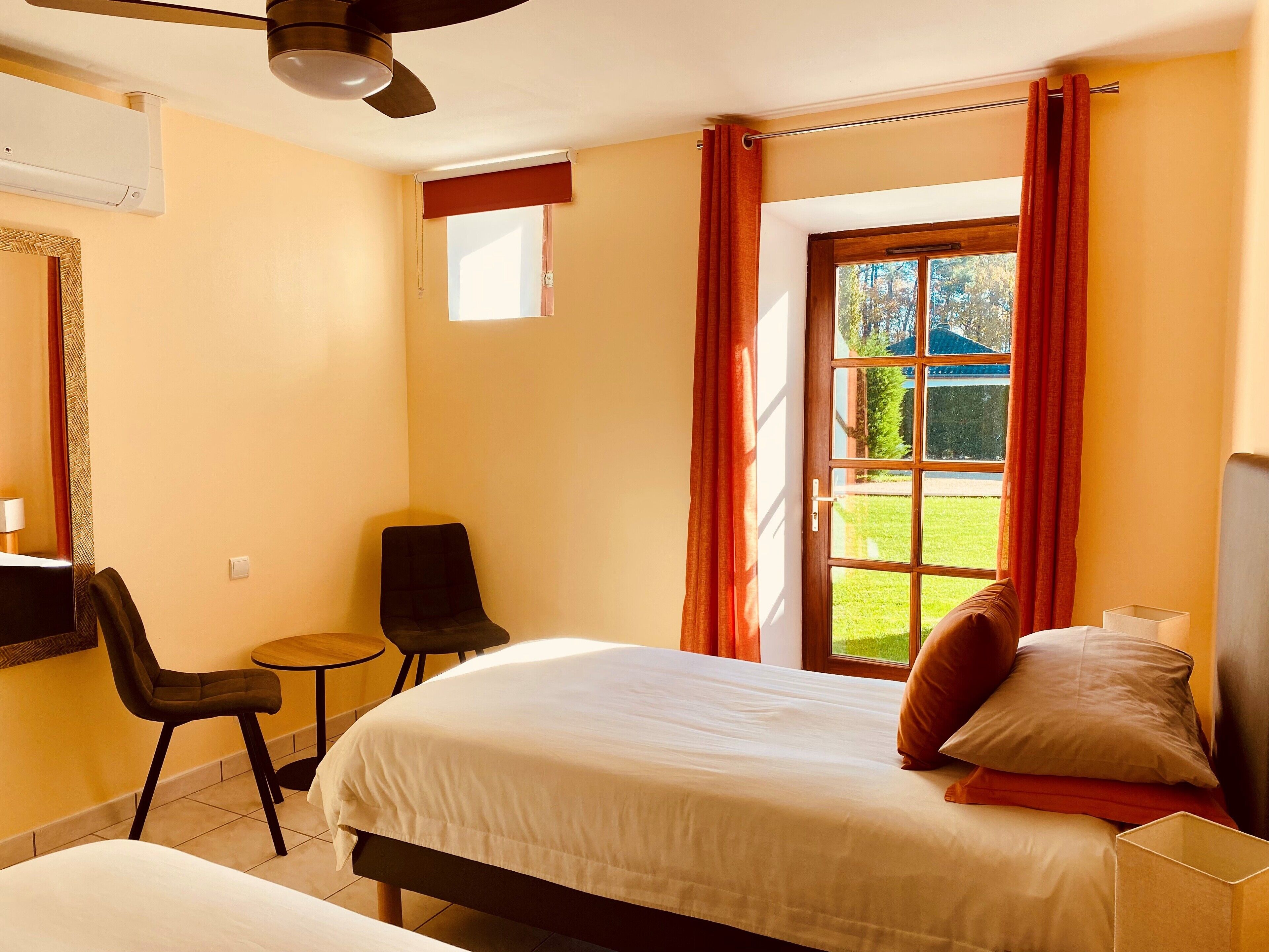 A hotel room with a bed, a chair, a small table, a mirror, and a window with curtains.