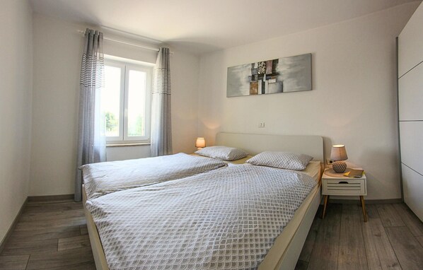 A double bed with a patterned bedspread, two bedside lamps, a small bedside table, and a window with curtains. - Awesome apartment in Lovrecica with WiFi (Lovrecica)