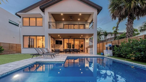 Et moderne hus med to etager, en swimmingpool, udendørs møbler og en balkon.