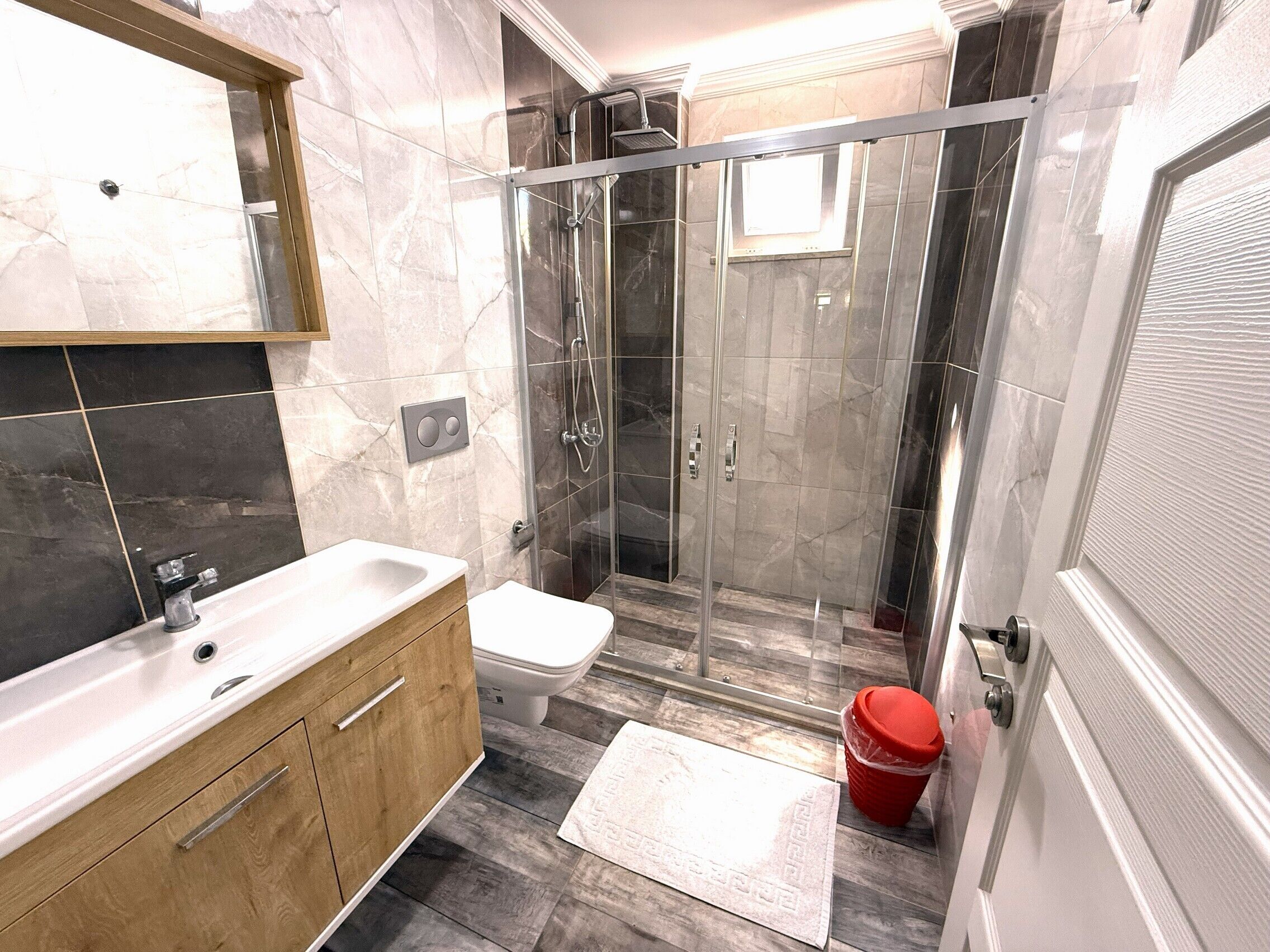 A modern bathroom with a glass-enclosed shower, a wooden vanity, a white sink, and a toilet.