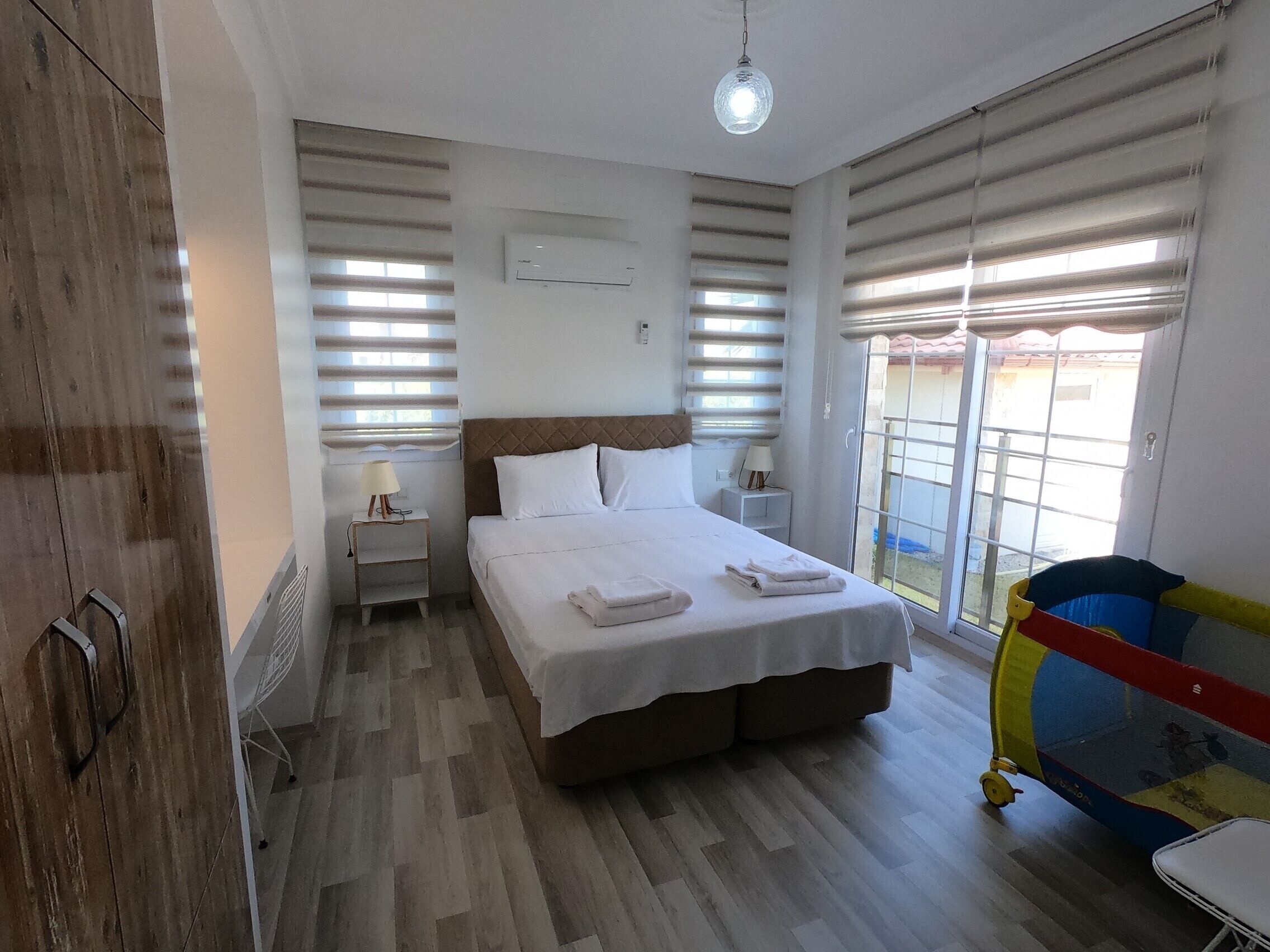 Une chambre d’hôtel avec un lit, des tables de chevet, une lampe et une fenêtre avec des stores.