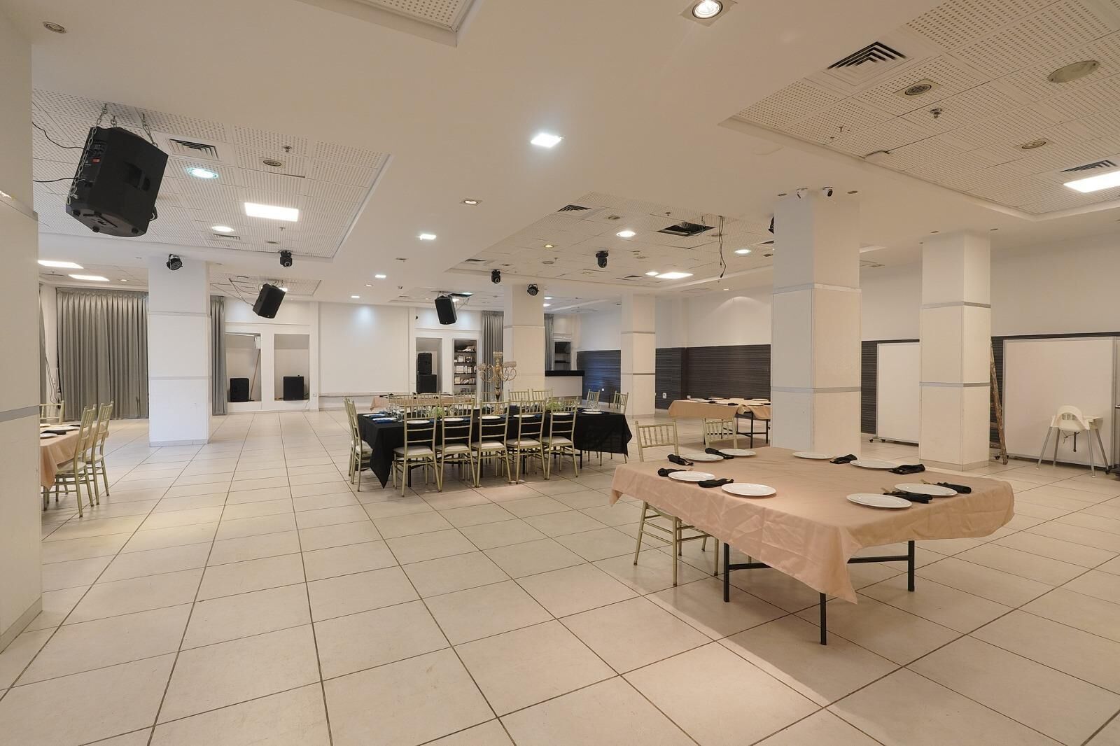 A spacious conference room with multiple tables, chairs, and a stage with a projector.