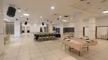 Una espaciosa sala de conferencias con múltiples mesas, sillas y un escenario con proyector.