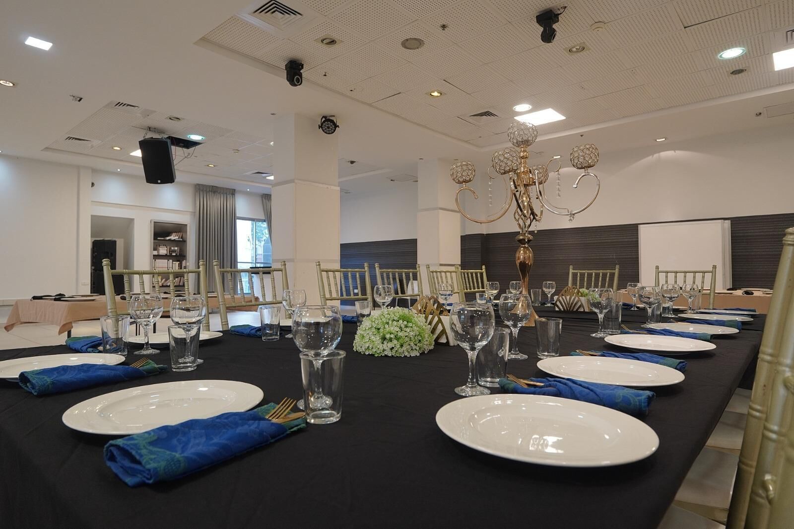 A conference room with a long table set for a formal event, equipped with chairs, plates, glasses, and a decorative centerpiece.