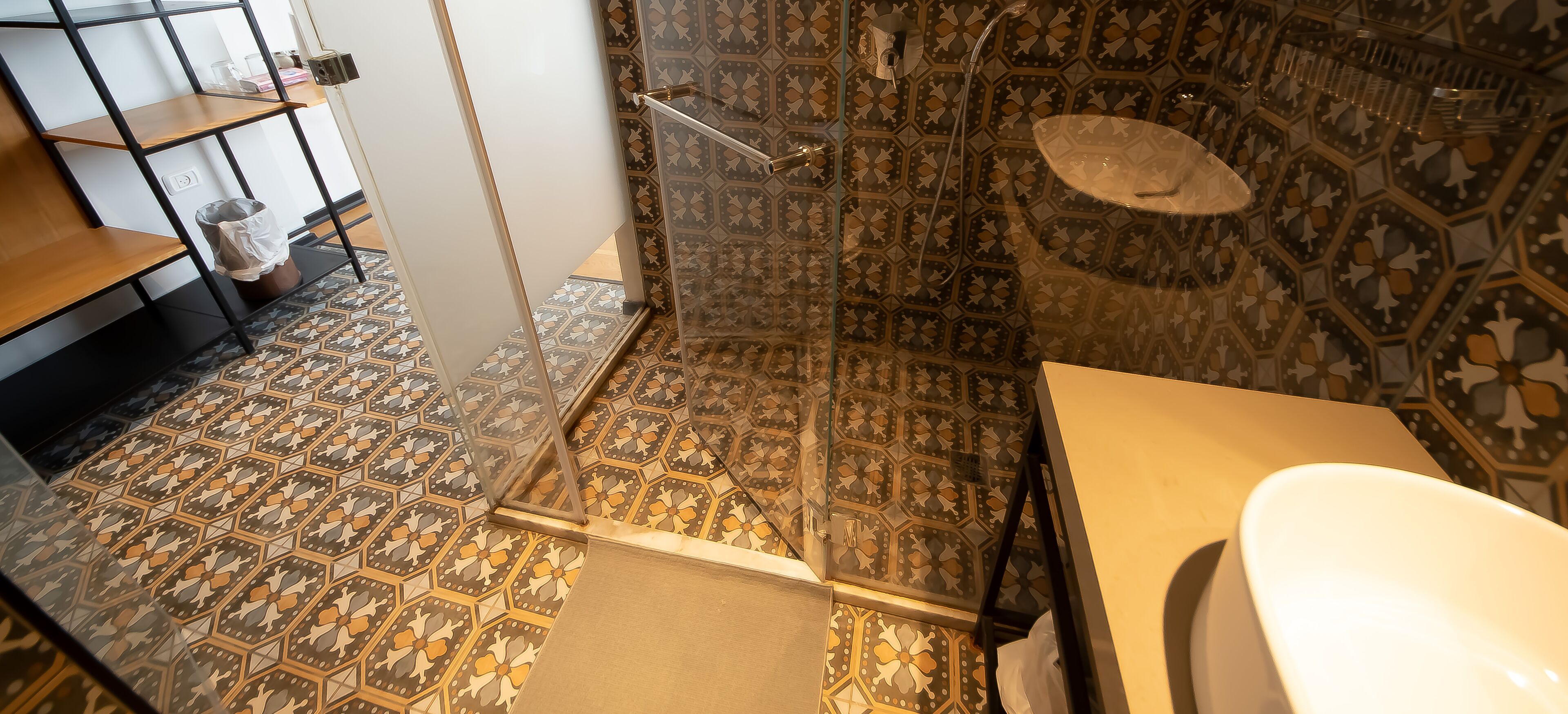 A bathroom with a patterned floor, a shower with a glass door, and a white sink.