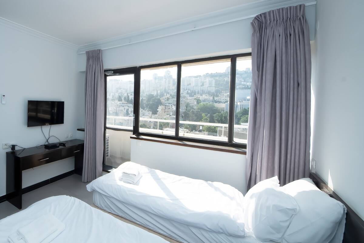 Una habitación de hotel con cama, televisor, ventana con cortinas y vista a la ciudad.