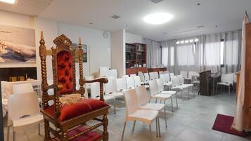 Una habitación de hotel con una cama grande, una silla de madera, sillas blancas, una estantería y un escritorio.