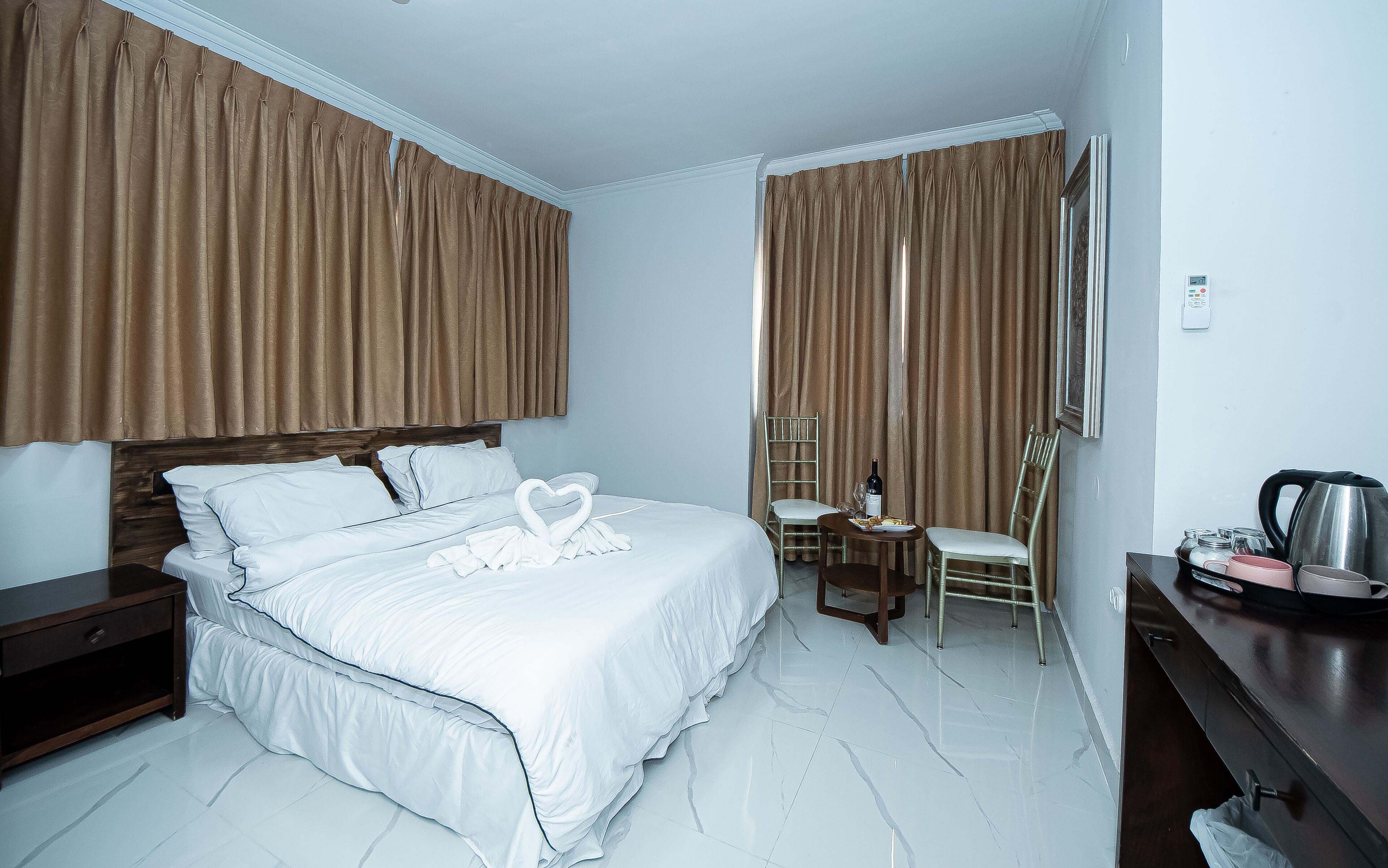 Une chambre d’hôtel avec un grand lit, un bureau avec une bouilloire, une chaise et une petite table sur laquelle se trouve une bouteille de vin.