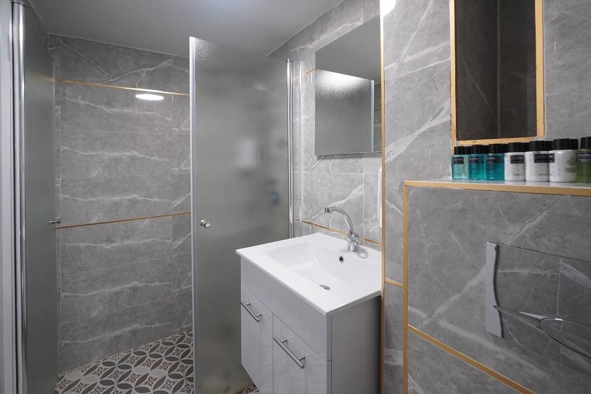 Un baño moderno con ducha de vidrio, un lavabo blanco y paredes de mármol.