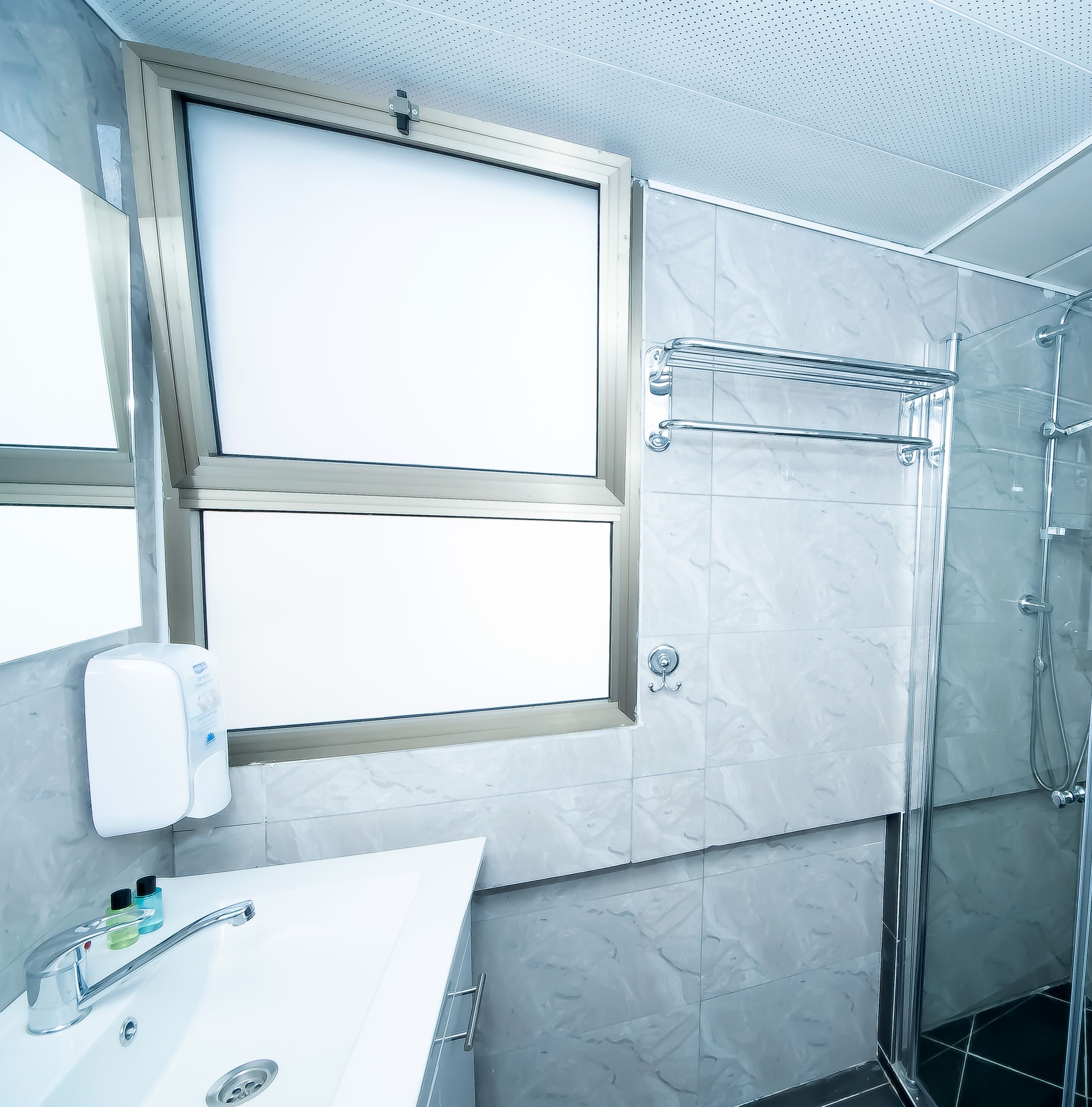 A modern bathroom with a large mirror, a shower with a glass door, and a sink with a soap dispenser.