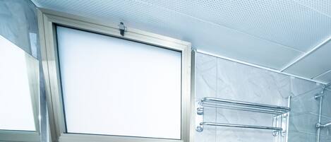 A modern bathroom with a large mirror, a shower with a glass door, and a sink with a soap dispenser.