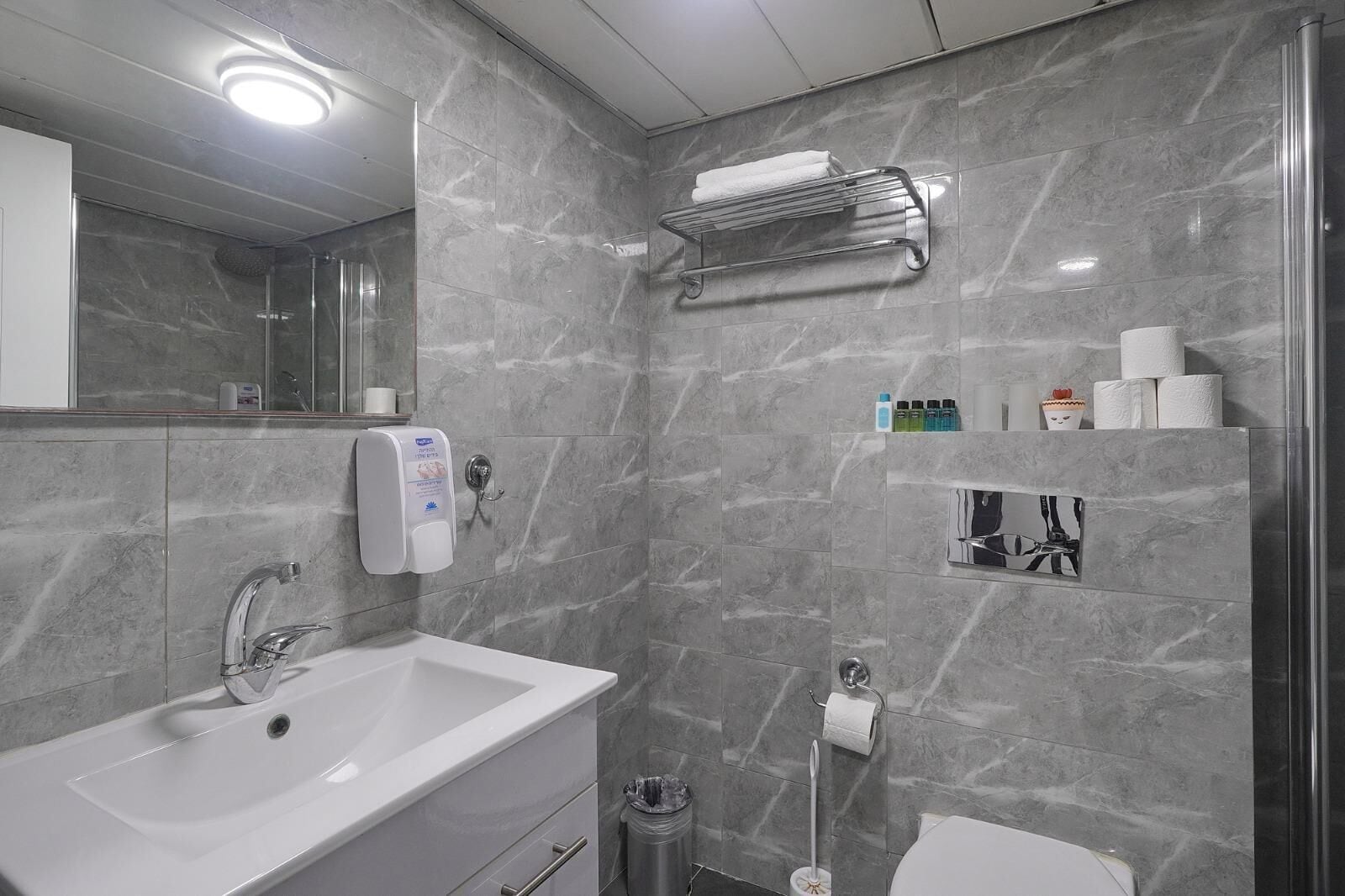 A modern bathroom with a white sink, a handheld showerhead, a towel rack, and a toilet.