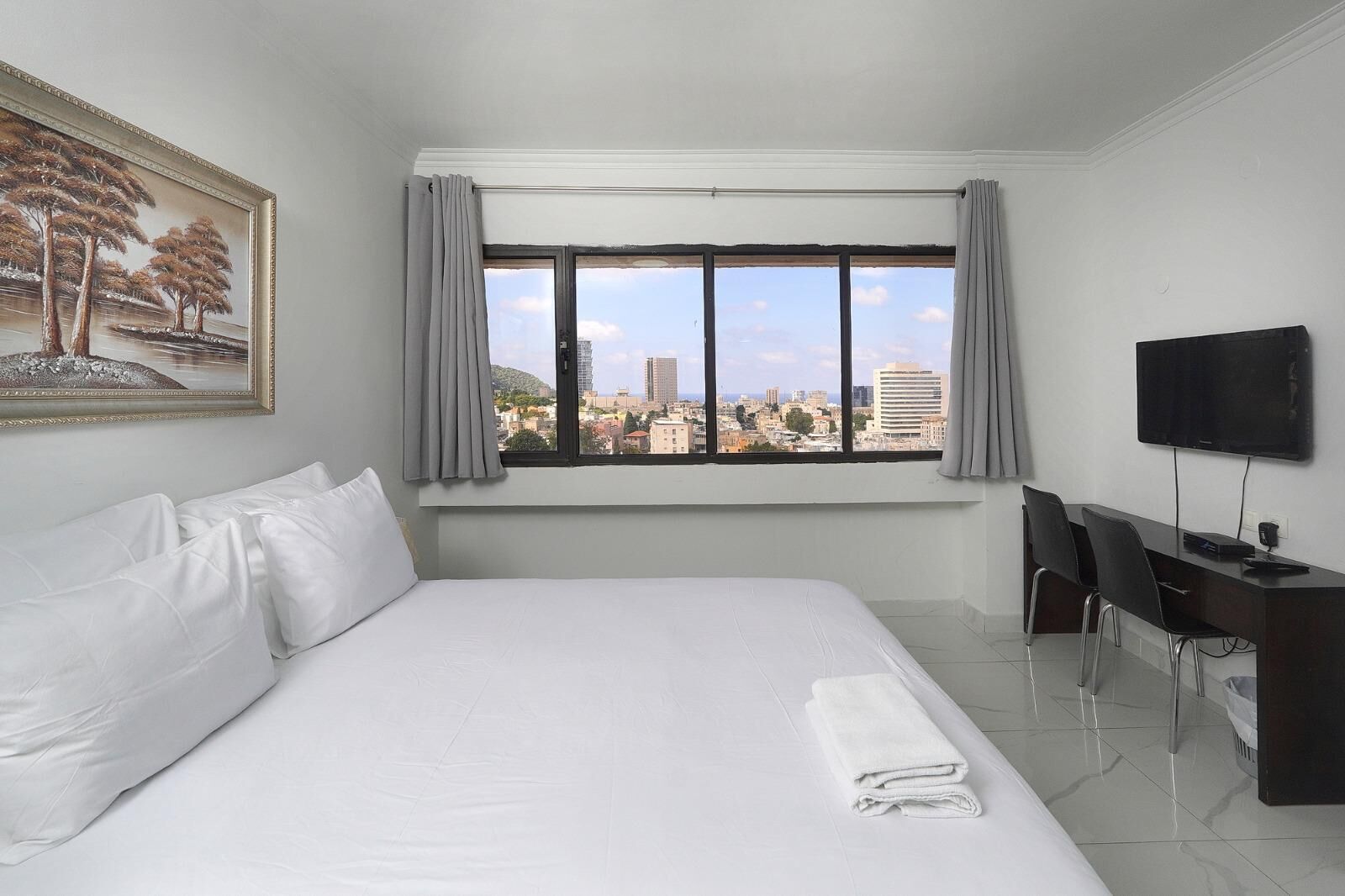Habitación de hotel con una cama grande, un escritorio con sillas, un televisor y una ventana con vista a la ciudad.