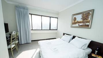 A hotel room with a bed, a desk with a chair, a TV, and a painting on the wall.