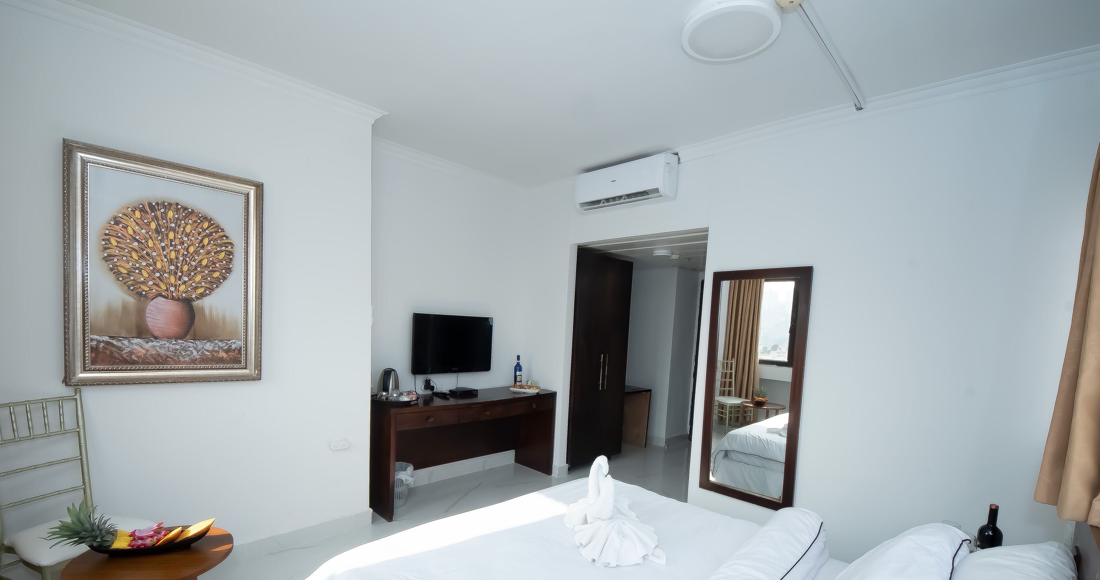 Quarto de hotel com uma cama, uma escrivaninha com televisão de tela plana, um espelho e ar condicionado fixado na parede.