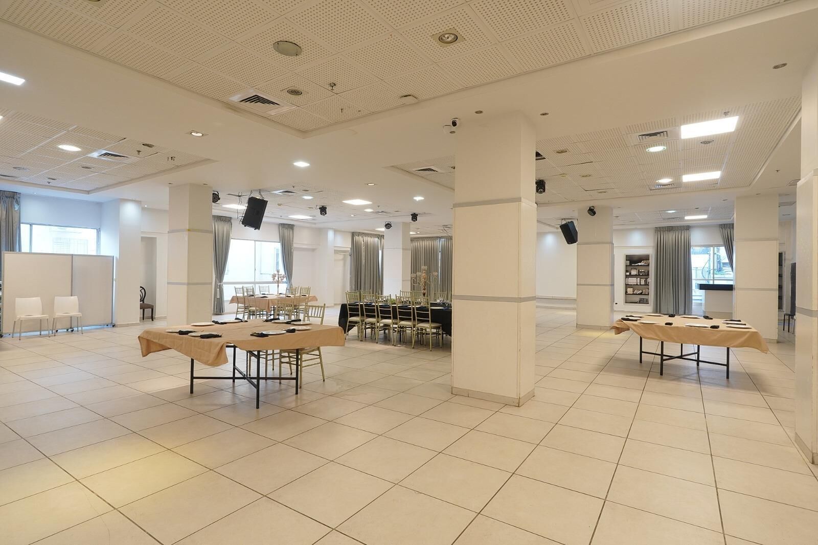 Una amplia sala de conferencias con varias mesas y sillas, ventanas grandes y suelo de baldosas.
