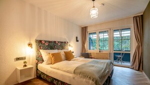 Une chambre à coucher avec un lit, des tables de chevet, une fenêtre avec des rideaux et une vue sur la verdure.