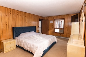 Ein Schlafzimmer mit einem Bett, Holzwänden, einem Fenster, einem Schminktisch und einem Nachttisch.