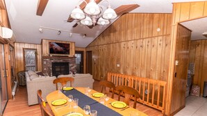 Een eetgedeelte met een lange houten tafel gedekt voor zes personen, een open haard en een bankstel op de achtergrond.
