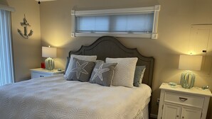 Ein ordentlich bezogenes Bett mit sternförmigen Kissen, einer Nachttischlampe und einem Nachttisch mit einer Dekoration.