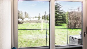Vista a través de una puerta de cristal de un área exterior con césped, una cerca de metal, una estructura de piedra y árboles.