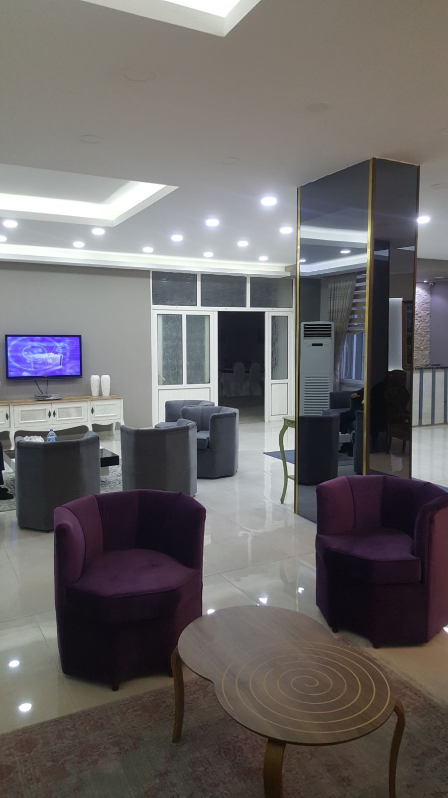 A modern living room with a flat-screen TV, comfortable seating, and a large mirror.