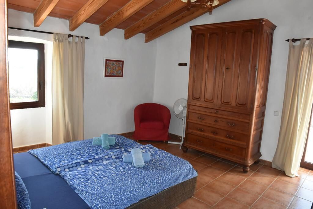 A bedroom with a bed, a red chair, a wooden cabinet, and a window with curtains.
