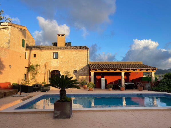 A pool area with a building, outdoor seating, and a covered patio.