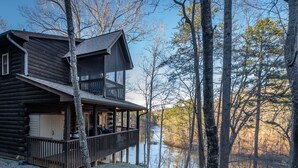 A log cabin with a balcony overlooking a lake, surrounded by trees. - Beautiful Lake Front Log Cabin with Dock  (Mill Spring)