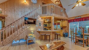 A spacious wooden interior with a high ceiling, a staircase, a kitchen area, and a dining setup. - Beautiful Lake Front Log Cabin with Dock  (Mill Spring)