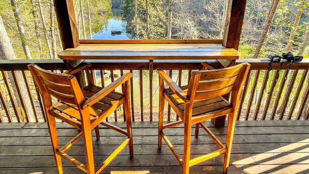 A wooden deck with a table and two chairs, overlooking a forested area with a lake. - Beautiful Lake Front Log Cabin with Dock  (Mill Spring)