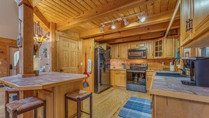 A wooden cabin interior with a kitchen featuring wooden cabinets, a refrigerator, a stove, and a bar area with stools. - Beautiful Lake Front Log Cabin with Dock  (Mill Spring)