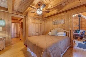 A wooden cabin bedroom with a bed, a ceiling fan, and a visible fireplace.